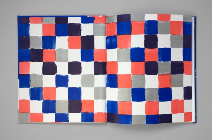 Open book with a pattern of square color fields in blue, red, gray, and white.